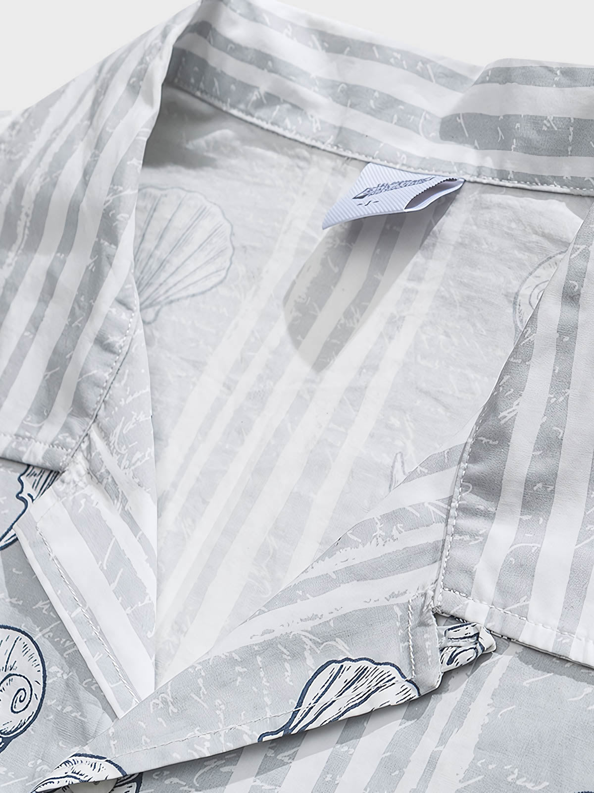 貝殻プリント半袖シャツの精巧なプリントパターンのクローズアップ。繊細な工芸技術と高品質の純綿素材が、快適な着用体験を実現します。