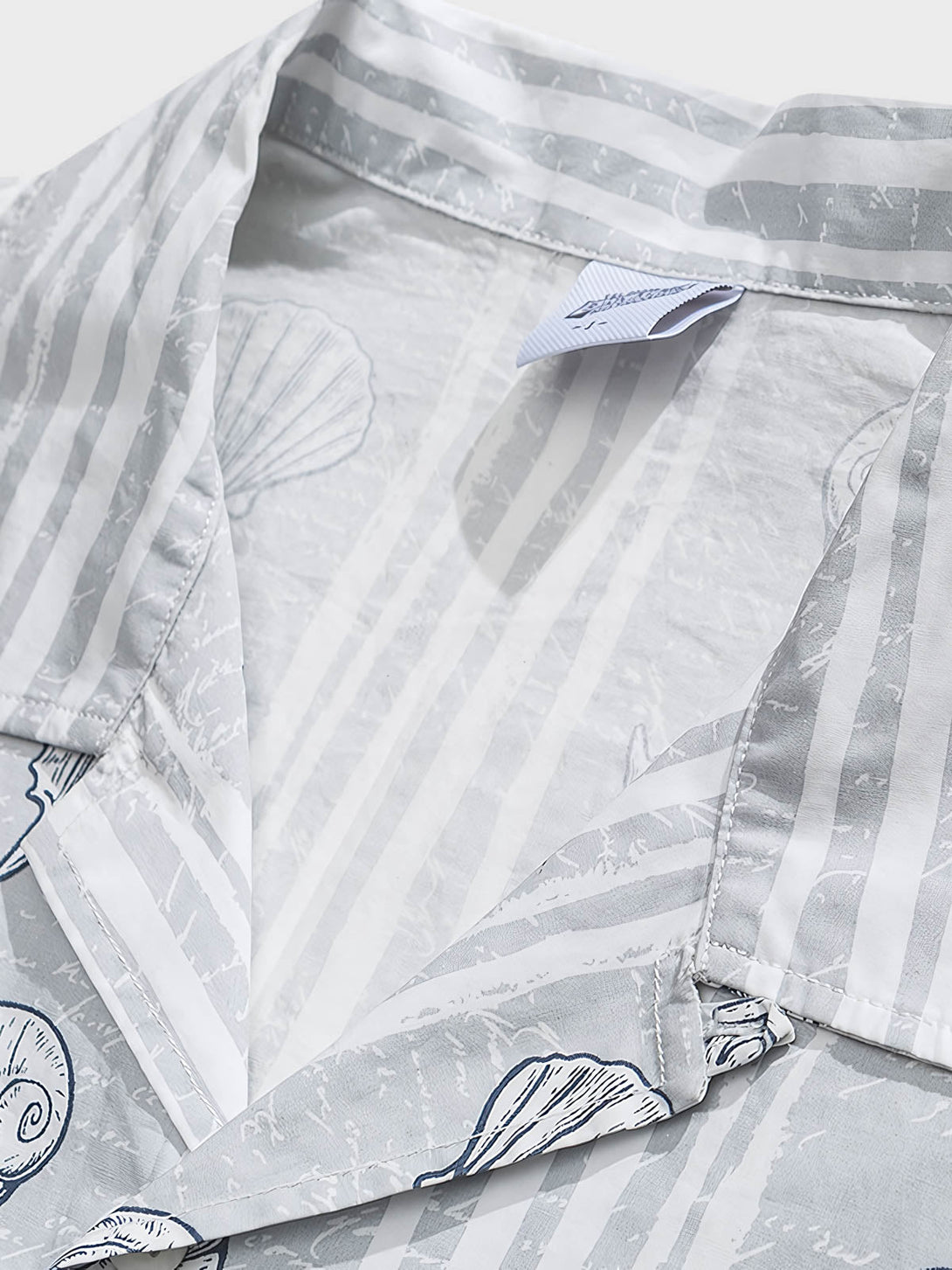 貝殻プリント半袖シャツの精巧なプリントパターンのクローズアップ。繊細な工芸技術と高品質の純綿素材が、快適な着用体験を実現します。