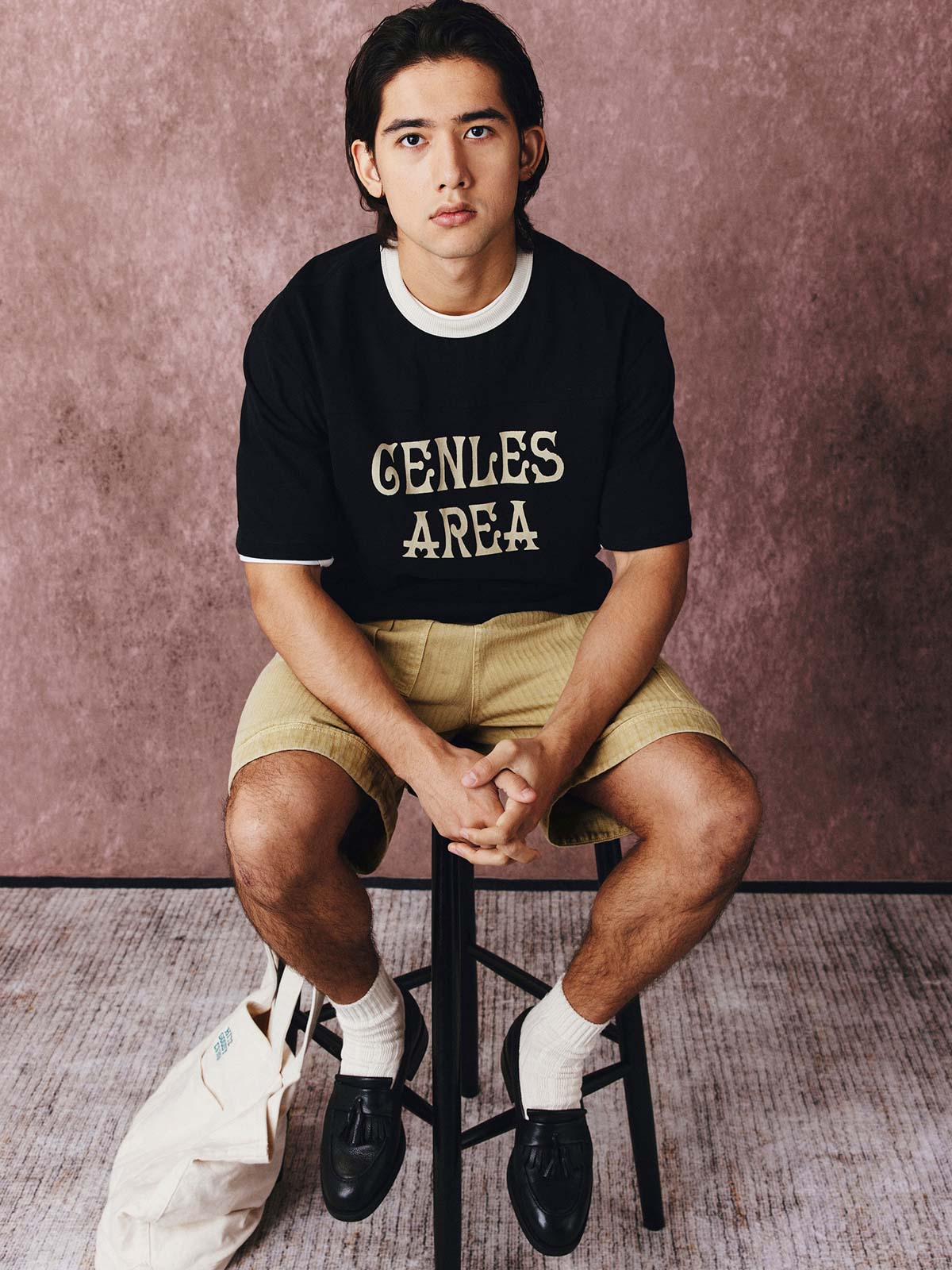 モデルがフットボールカルチャープリントTシャツを着用し、ジンジャーイエローのバリエーションで、ダークカラーのカジュアルパンツとスポーツシューズを合わせたカジュアルなスタイリングでポーズをとる画像。レトロかつ現代的な夏の装いを演出。